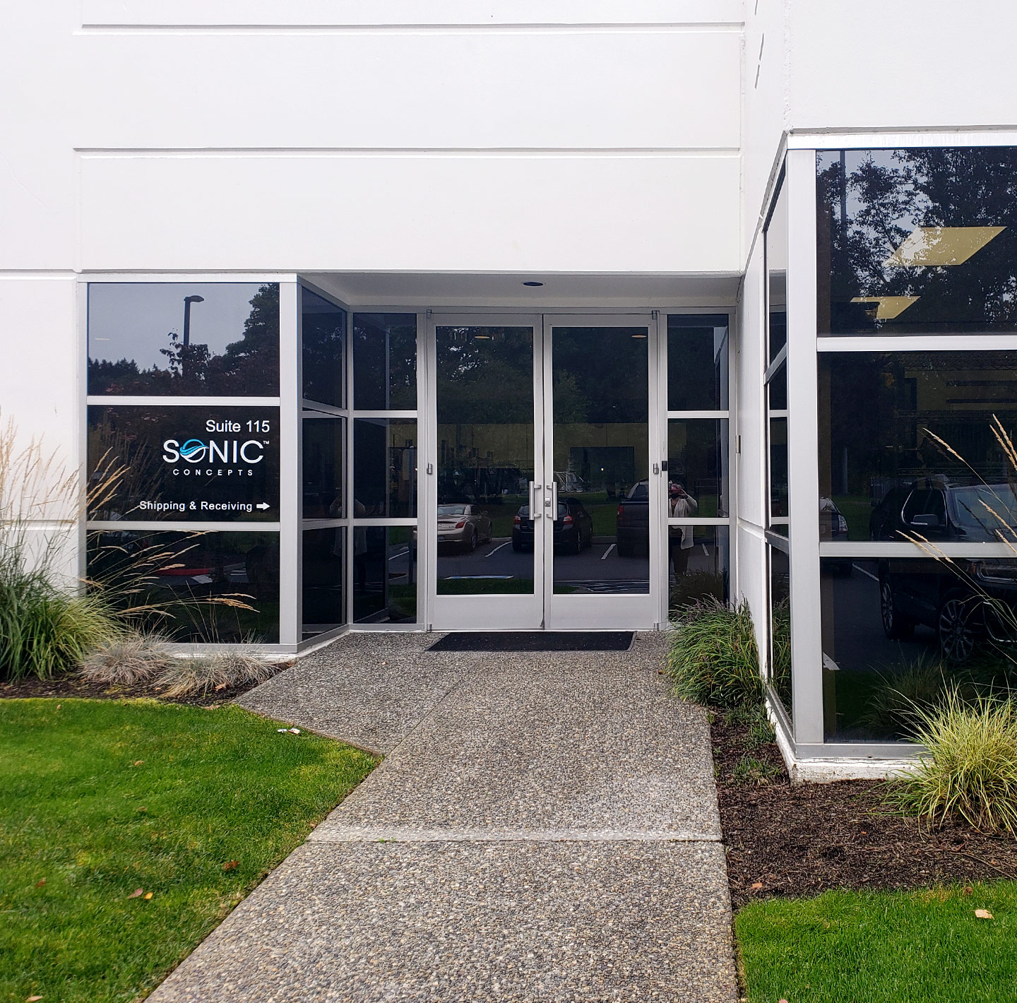 Modern glass-front building with concrete walkway and green lawn landscaping